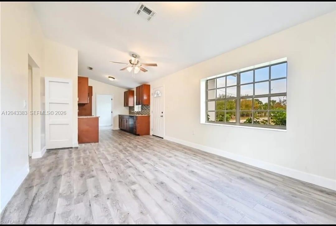 An open-concept room features light wood-look flooring, white walls, a ceiling fan, and a kitchen — 2830 NE 4th Ave, Naples FL 34120, NAPLES, FL
