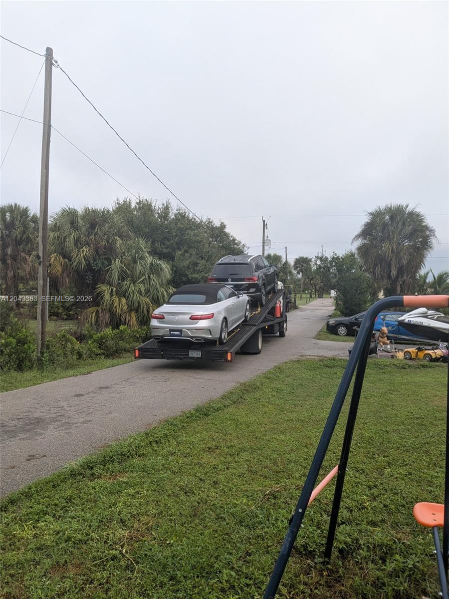 A car carrier trailer transports two vehicles along a paved driveway near palm trees — 2830 NE 4th Ave, Naples FL 34120, NAPLES, FL