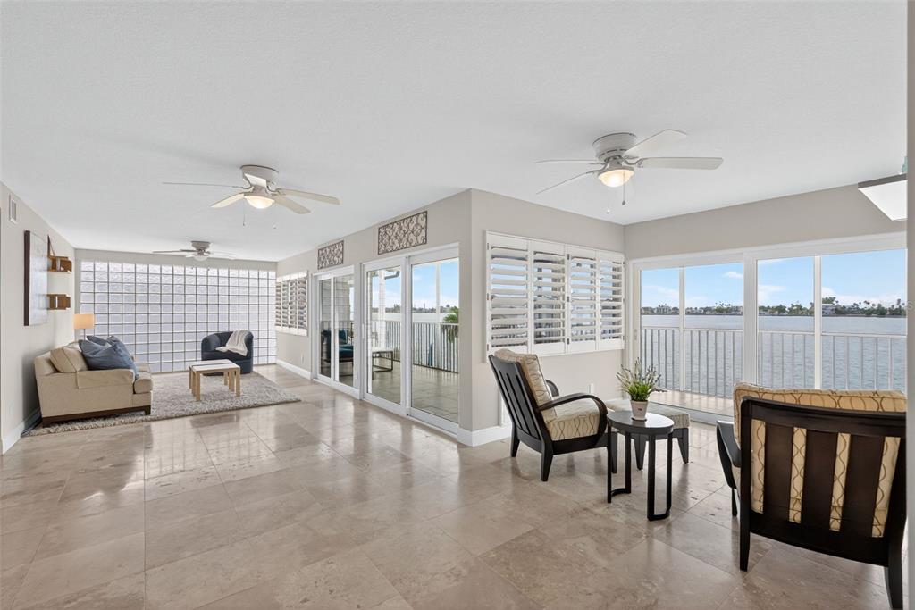 A spacious living area with tile floors, ceiling fans, and large windows overlooking the water — 800 MADONNA BOULEVARD UNIT 1, TIERRA VERDE, FL