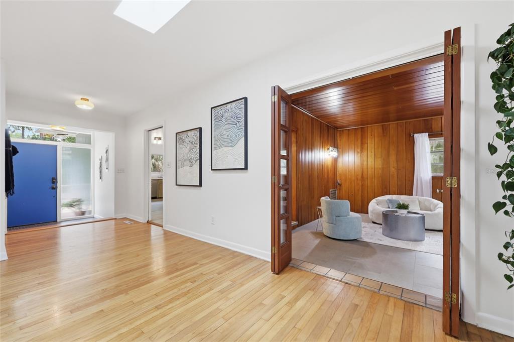 A room with hardwood floors leads to a wood-paneled den through open French doors — 616 SW 21ST AVENUE, GAINESVILLE, FL