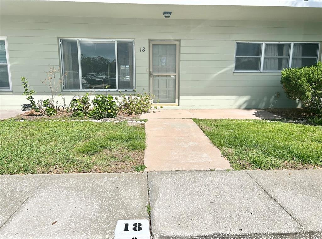 The exterior of a single-story residential unit features light green siding, a front door, and windows — 2400 COLUMBIA DRIVE UNIT 18, CLEARWATER, FL