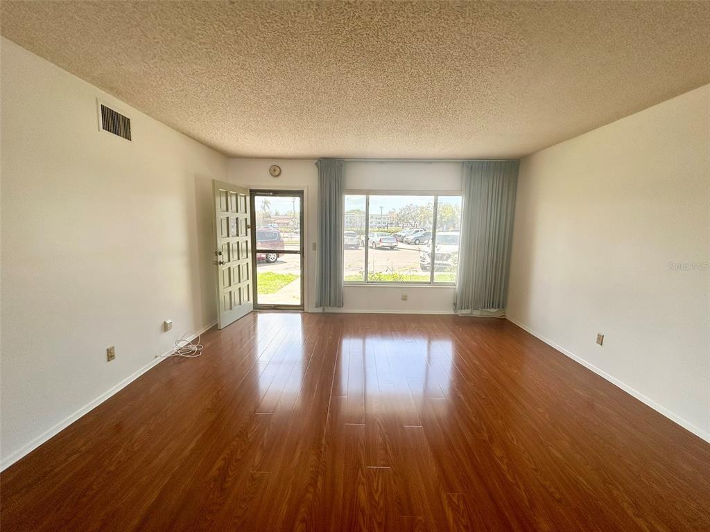 A living room features wood-look flooring, a textured ceiling, and a large window with curtains — 2400 COLUMBIA DRIVE UNIT 18, CLEARWATER, FL