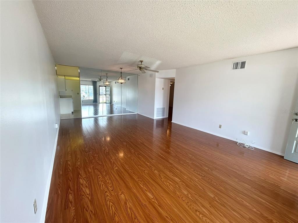 A living room with wood-look flooring, a ceiling fan, and a mirrored wall — 2400 COLUMBIA DRIVE UNIT 18, CLEARWATER, FL