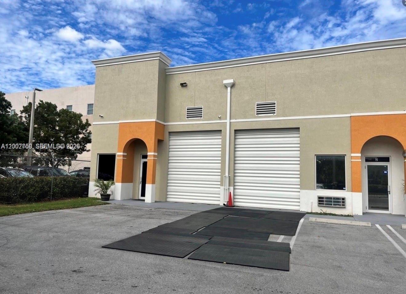 An exterior view of a commercial building with two roll-up doors and two glass entrances — 14911 SW 137th St, Kendall FL 33196, KENDALL, FL