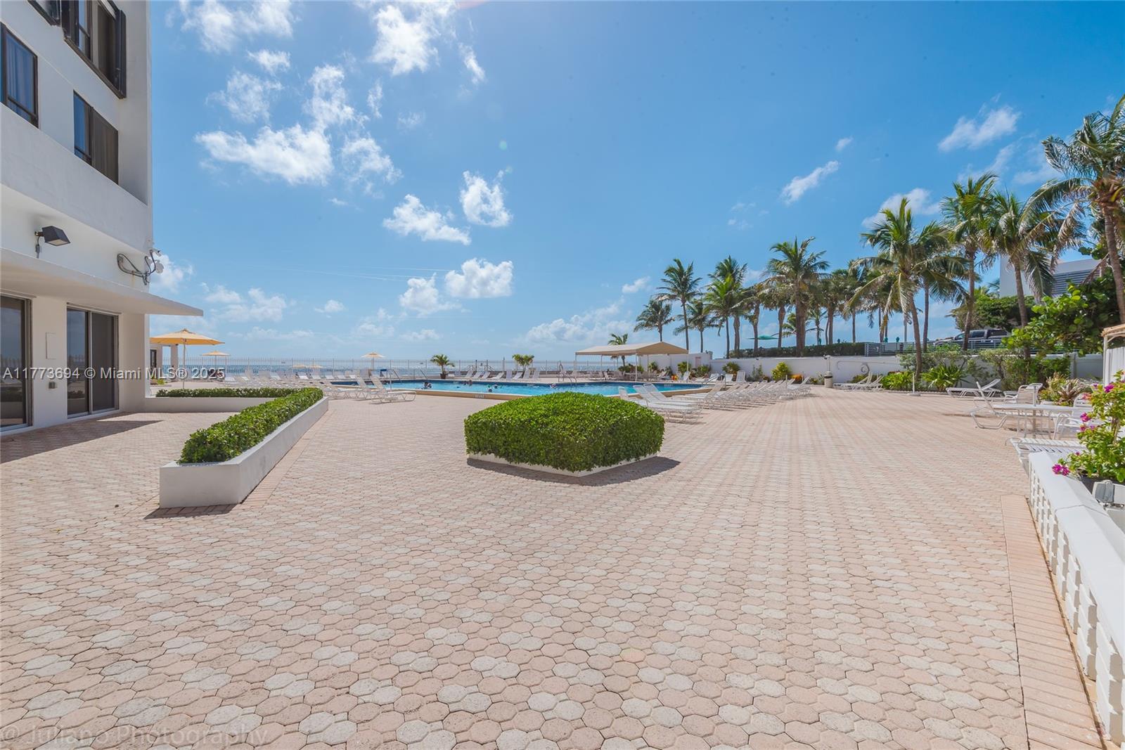 An outdoor pool deck features a swimming pool, lounge chairs, palm trees, and paved ground — 3505 S Ocean Dr # 504, Hollywood FL 33019, HOLLYWOOD, FL