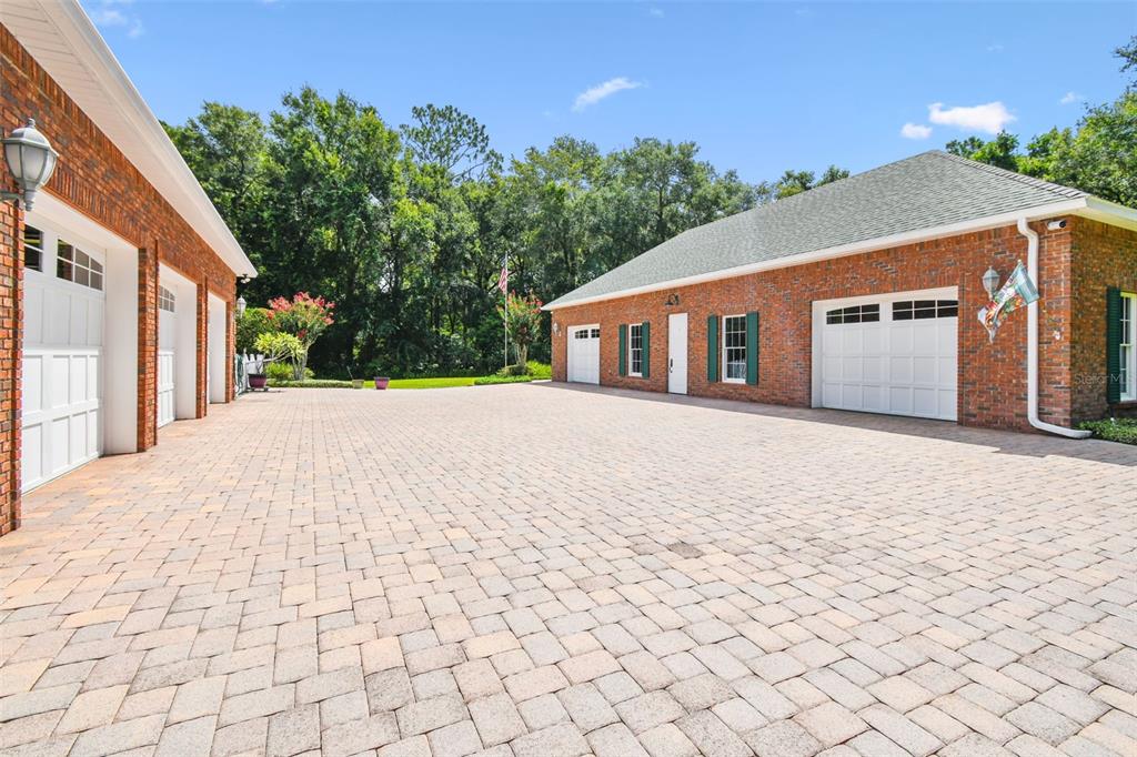 A large brick garage building with multiple white doors and green shutters faces a paved courtyard — 1745 TAYLOR WOODS ROAD, DELAND, FL