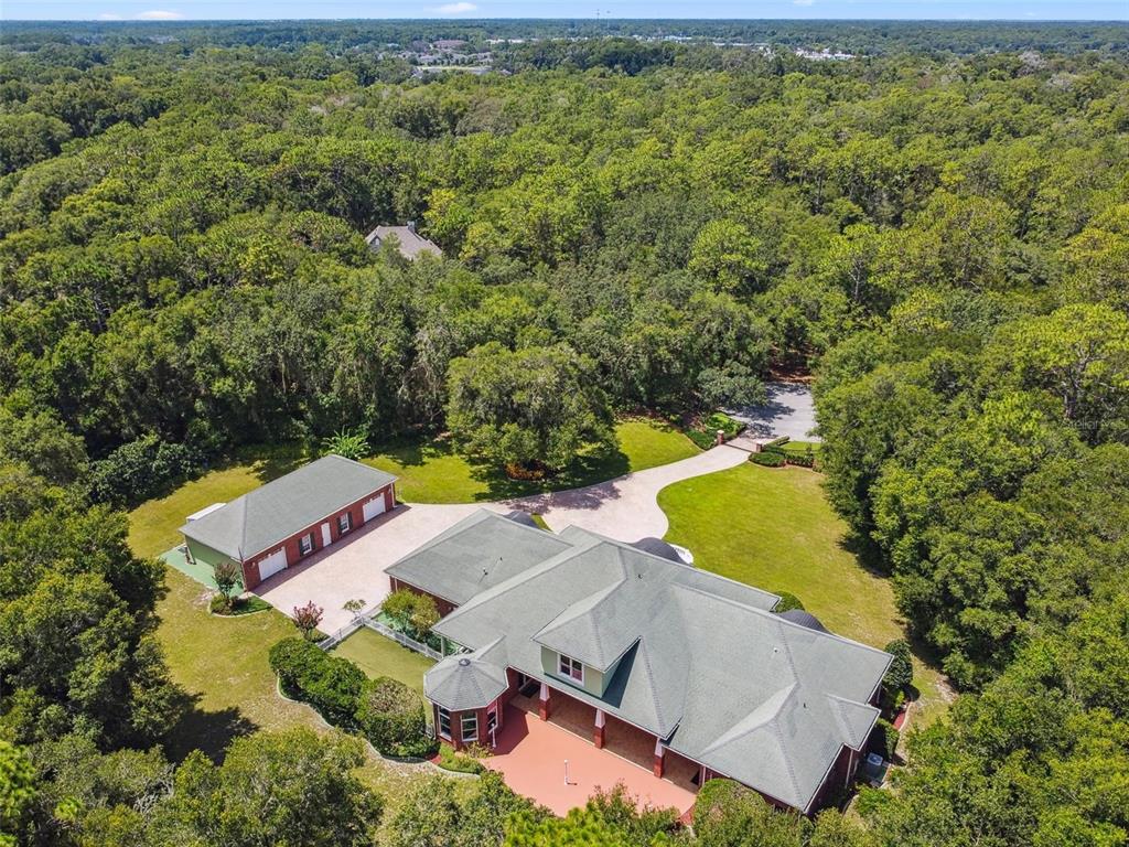An aerial view shows a house with a green roof, a detached garage, and surrounding woods — 1745 TAYLOR WOODS ROAD, DELAND, FL