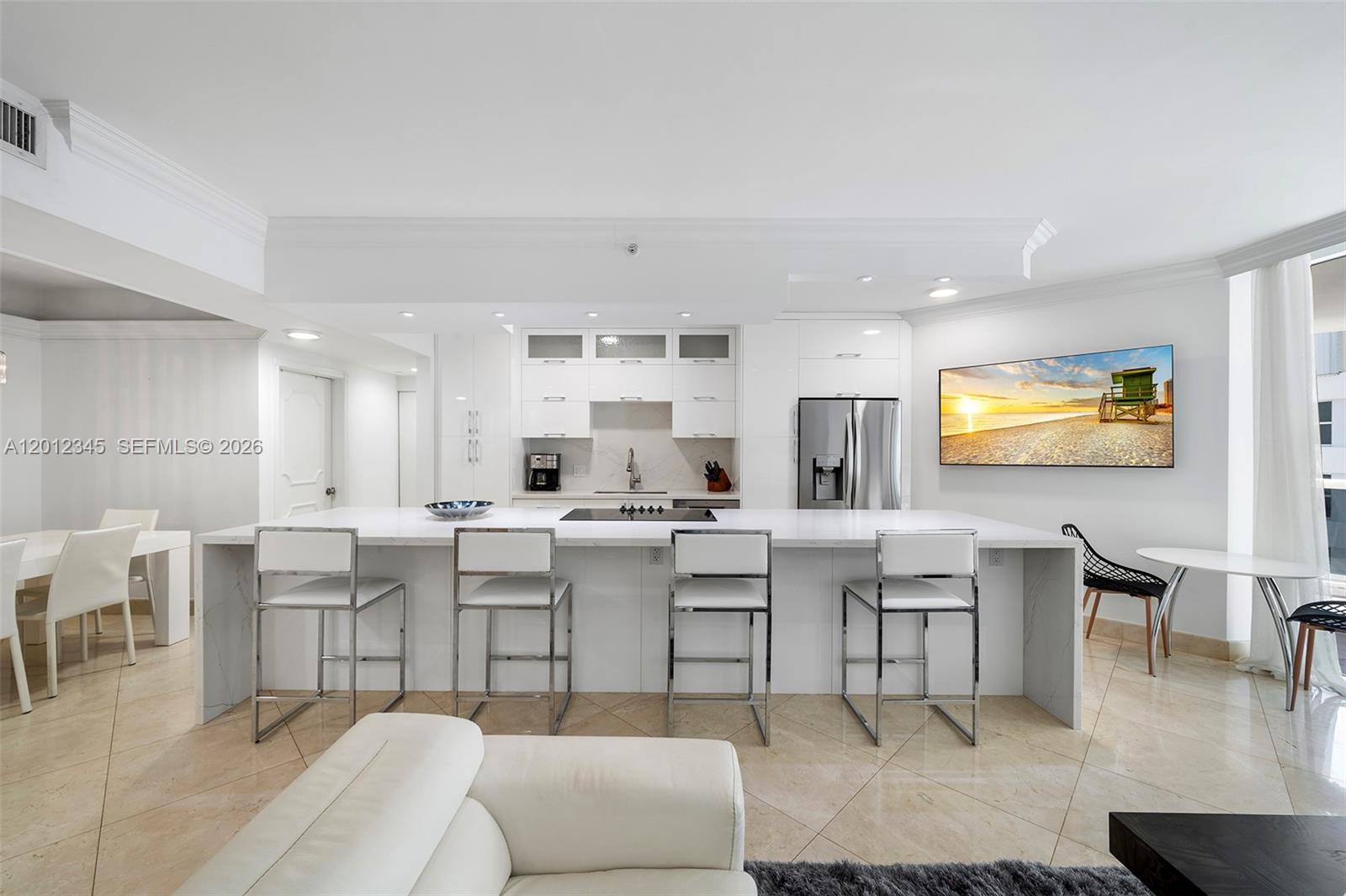 A modern kitchen features white cabinetry, a large marble-topped island, and four metal barstools — 4775 Collins Ave # 1504, Miami Beach FL 33140, MIAMI BEACH, FL
