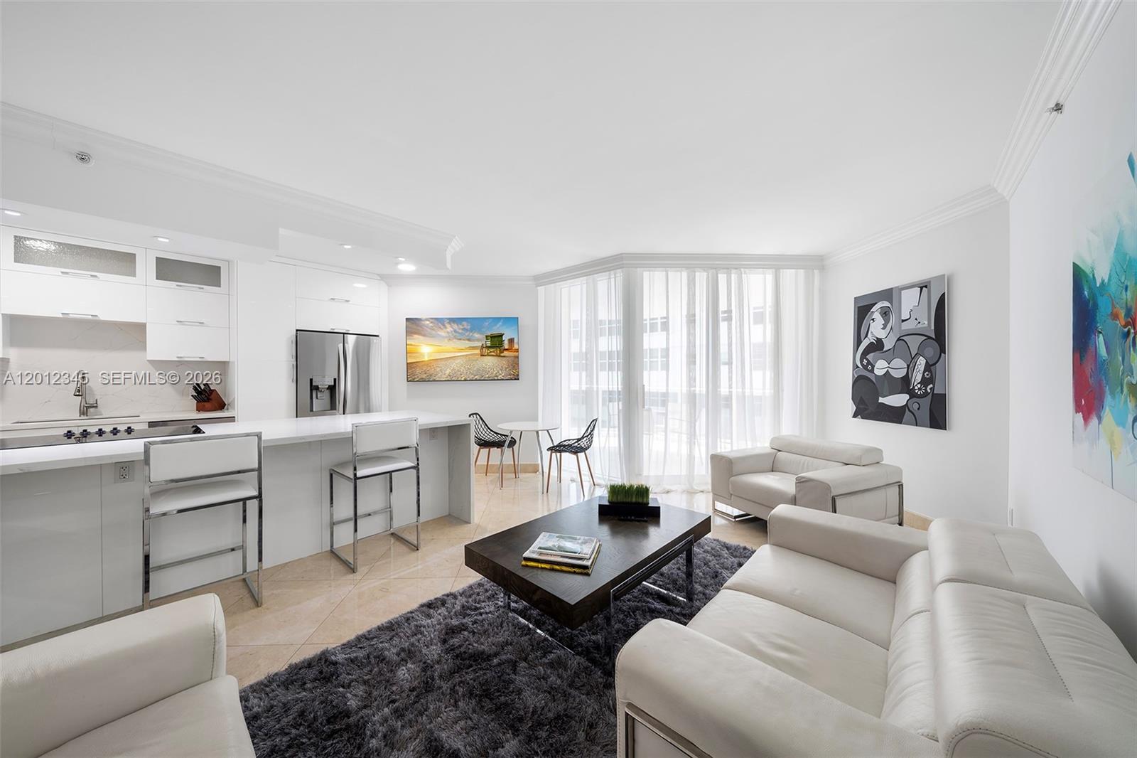 A modern open-concept living room and kitchen feature white cabinetry, tile flooring, and a rug — 4775 Collins Ave # 1504, Miami Beach FL 33140, MIAMI BEACH, FL