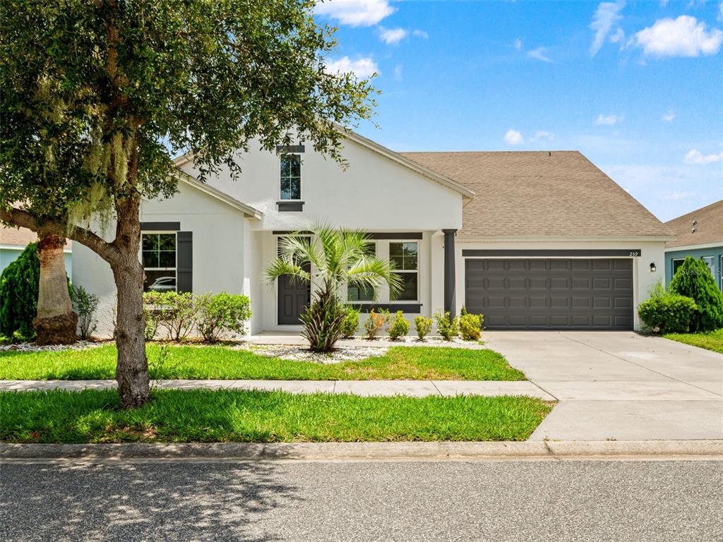 A single-story house with white stucco walls, a dark garage door, and a front lawn — 259 BLUE CYPRESS DRIVE, GROVELAND, FL