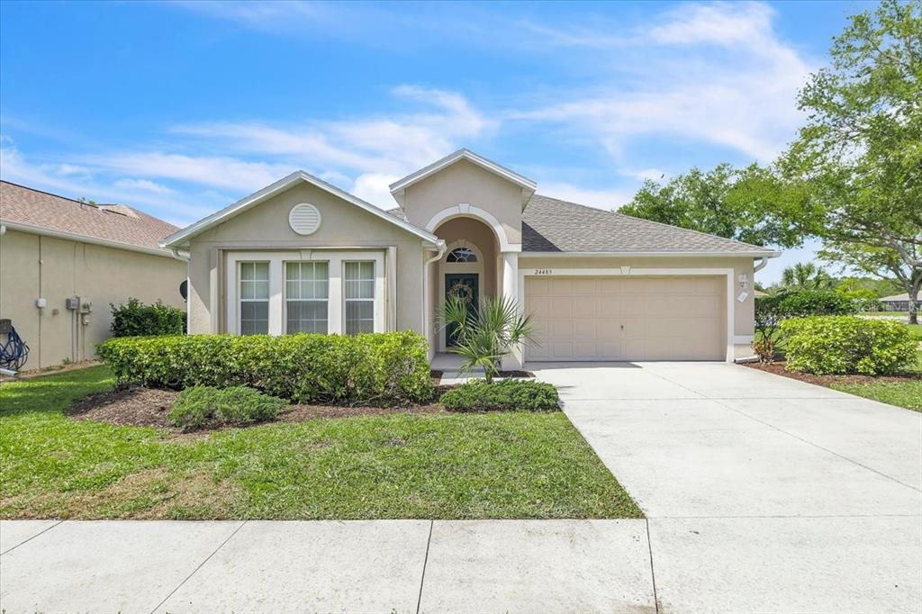 A single-story suburban house features a beige stucco exterior, a two-car garage, and landscaping — 24483 LAKESIDE MANOR, PORT CHARLOTTE, FL
