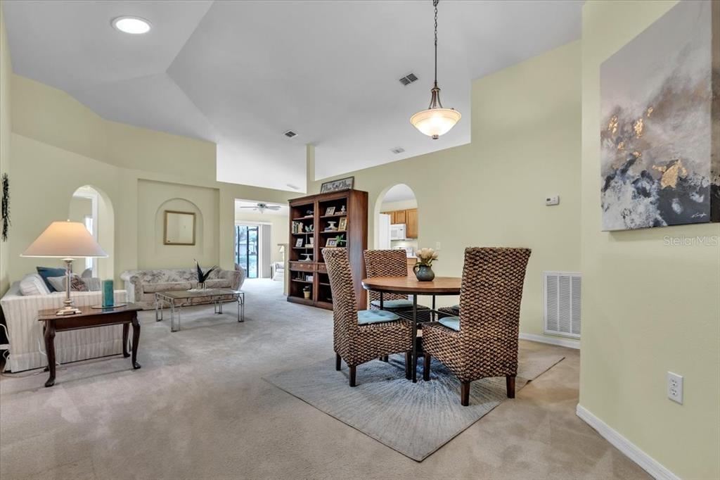 A living and dining area with vaulted ceilings, carpeted floors, and a wooden bookshelf — 24483 LAKESIDE MANOR, PORT CHARLOTTE, FL