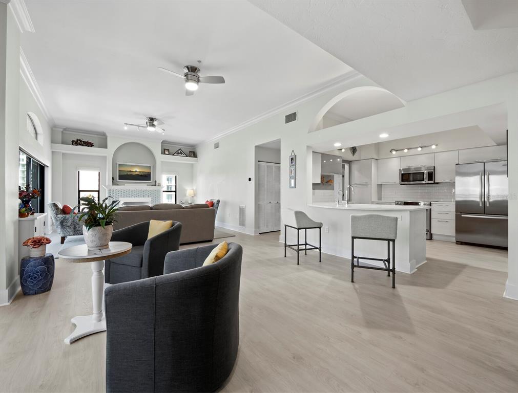 An open-concept living room and kitchen featuring light wood flooring, gray furniture, and stainless appliances — 205 GOLDEN GATE POINT UNIT 401, SARASOTA, FL