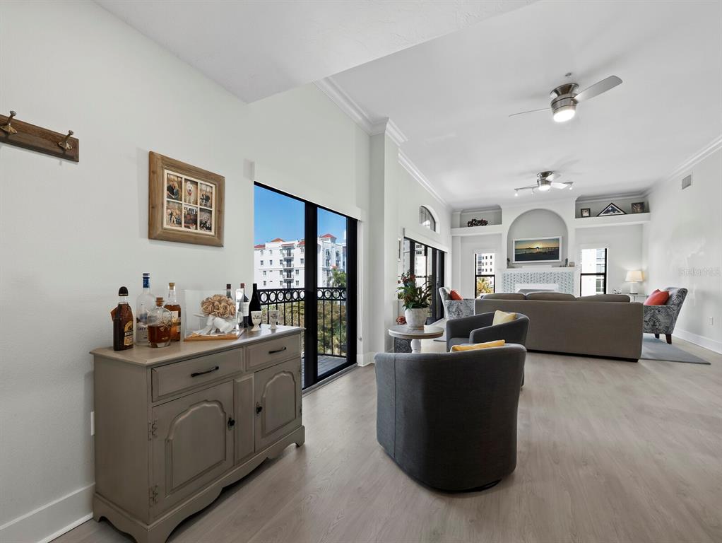 A living room features light wood flooring, a gray sideboard, and a view of buildings — 205 GOLDEN GATE POINT UNIT 401, SARASOTA, FL
