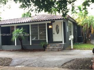 A single-story house with a dark exterior sits behind trees and a paved street — 335 NE 114th St, Miami FL 33161, MIAMI, FL