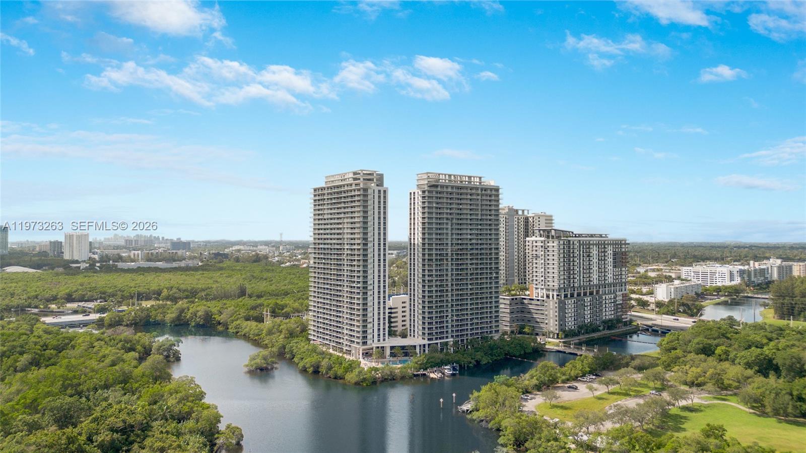 An aerial view shows two tall residential towers surrounded by a lake and greenery — 16385 Biscayne Blvd # 1502, North Miami Beach FL 33160, NORTH MIAMI BEACH, FL