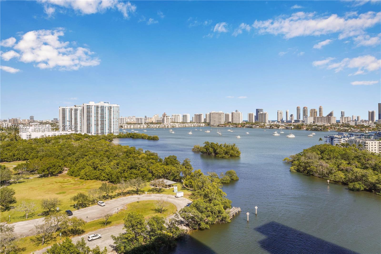 An aerial view shows a coastal waterway with boats, mangroves, and a distant city skyline — 16385 Biscayne Blvd # 1502, North Miami Beach FL 33160, NORTH MIAMI BEACH, FL