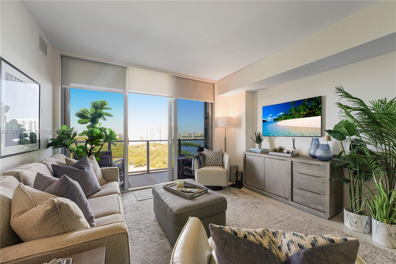 A living room features a sofa, ottoman, television, and a balcony with a water view — 16385 Biscayne Blvd # 1502, North Miami Beach FL 33160, NORTH MIAMI BEACH, FL