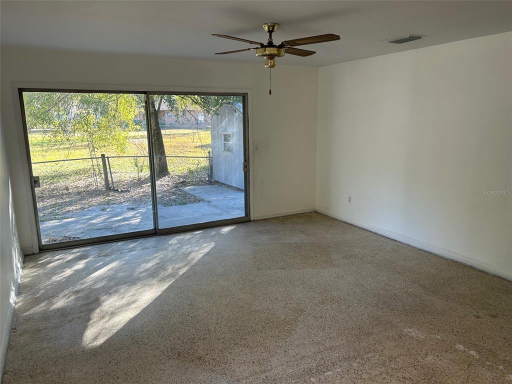An empty room features beige carpet, white walls, a ceiling fan, and sliding glass doors — 7001 32ND AVENUE S, TAMPA, FL