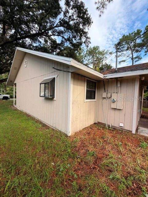 The exterior side of a tan house features vertical siding, a window, and utility equipment — 1427 ANNAPOLIS AVENUE, DAYTONA BEACH, FL