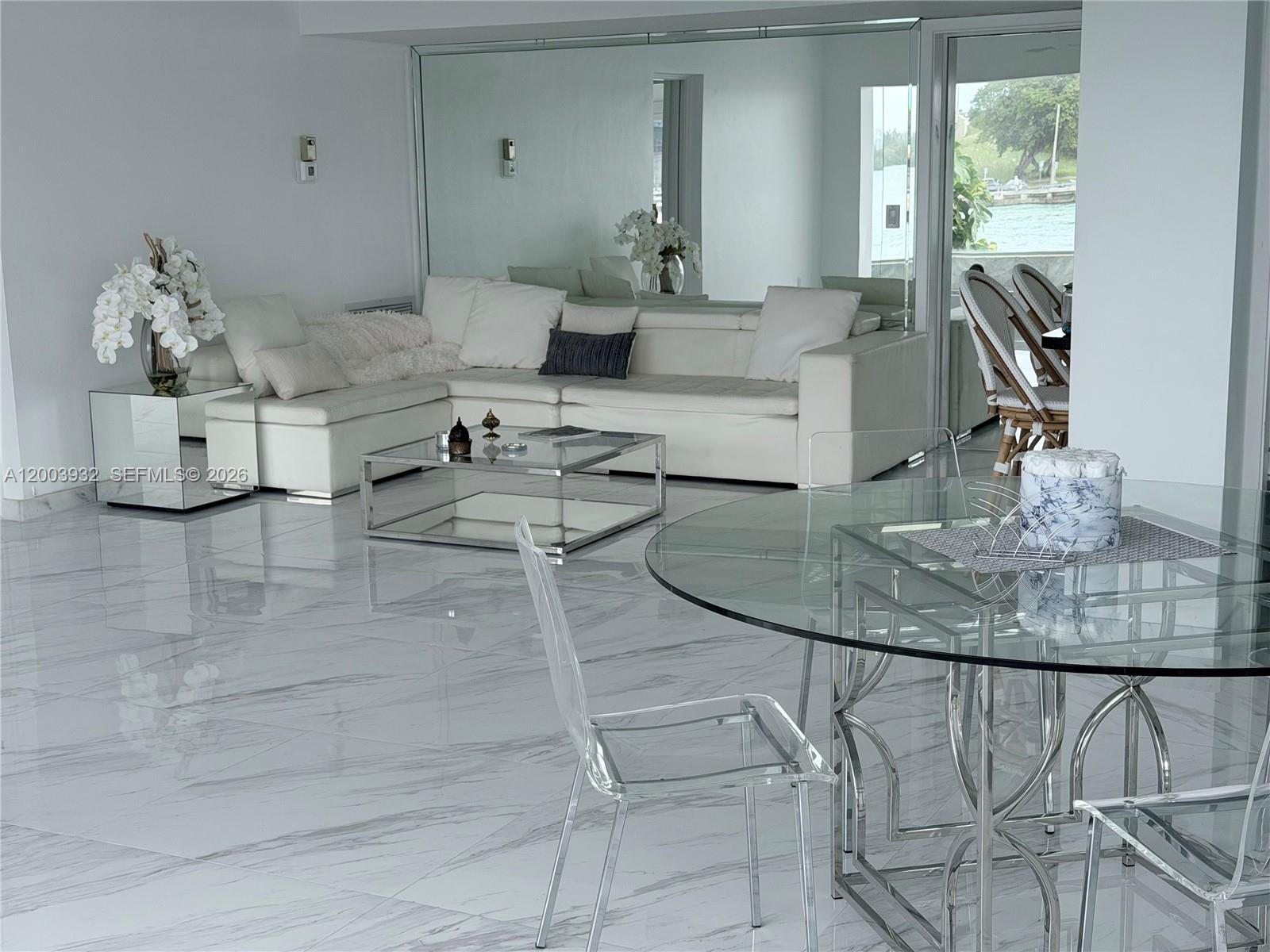 A modern living and dining area features white marble floors, a mirrored wall, and glass furniture — 286 Bal Bay Dr # 2B, Bal Harbour FL 33154, BAL HARBOUR, FL