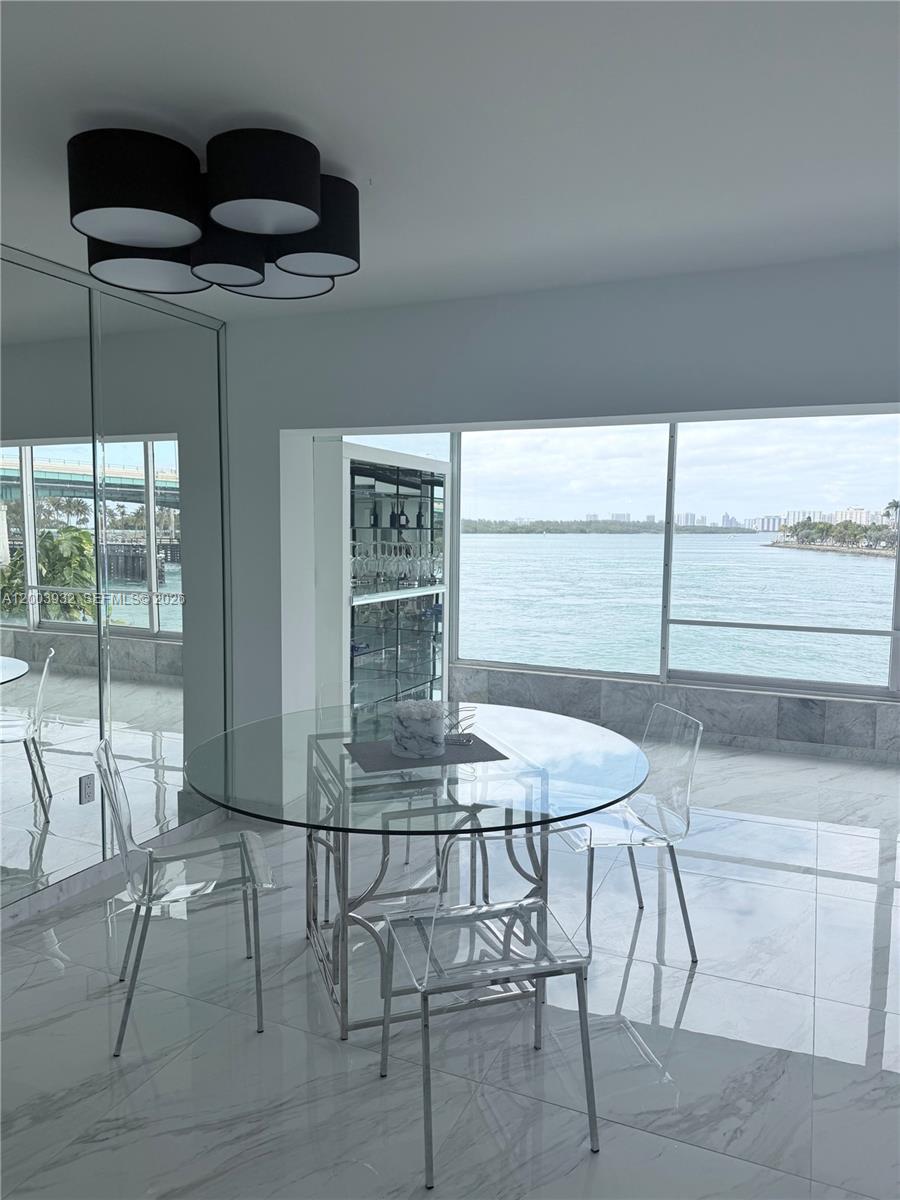 A dining area features a glass table, transparent chairs, marble floors, and a waterfront view — 286 Bal Bay Dr # 2B, Bal Harbour FL 33154, BAL HARBOUR, FL