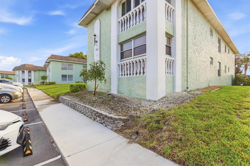 A light green multi-story apartment building with a stone retaining wall and parking lot — 1250 S PINELLAS AVENUE UNIT 214, TARPON SPRINGS, FL