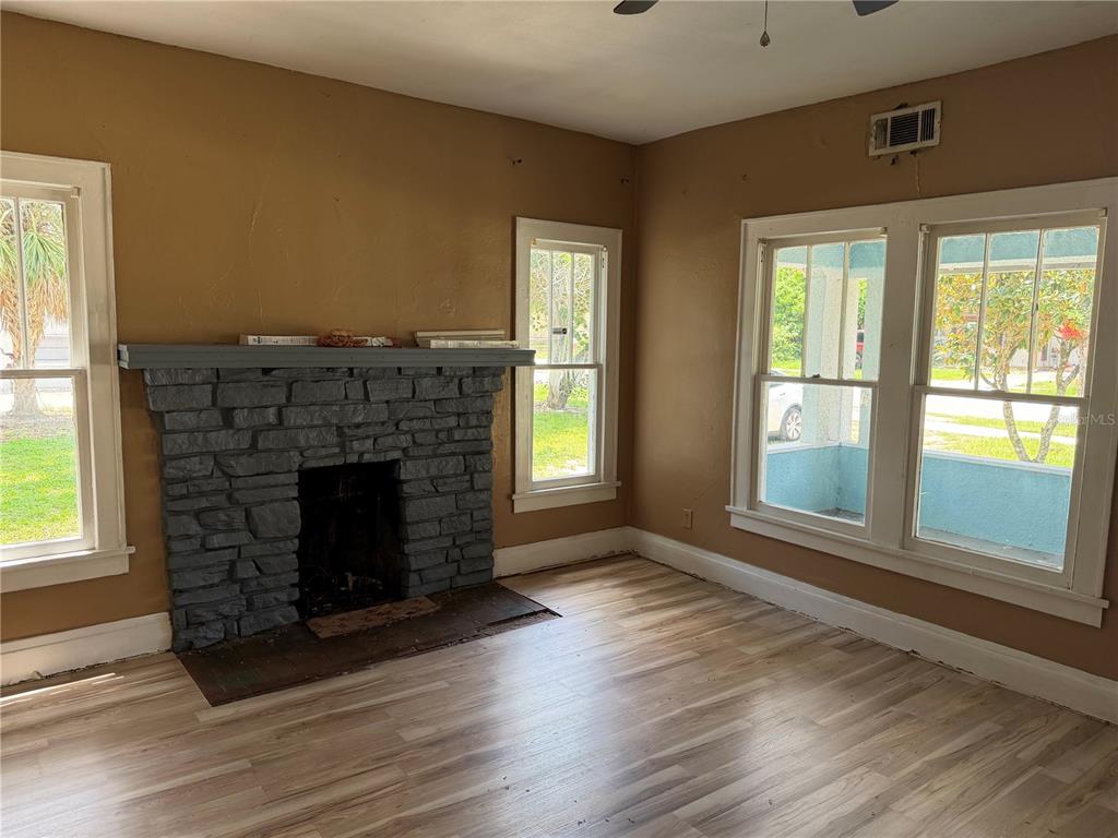 A living room features a stone fireplace, light wood-look flooring, and multiple windows — 444 AVENUE B NE, WINTER HAVEN, FL
