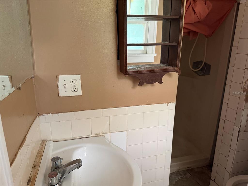 A bathroom features a white pedestal sink, tiled walls, a wooden shelf, and a mirror — 444 AVENUE B NE, WINTER HAVEN, FL