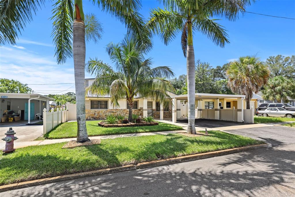 A single-story house with a stone facade, palm trees, and a carport under a blue sky — 2035 28TH STREET S, ST PETERSBURG, FL