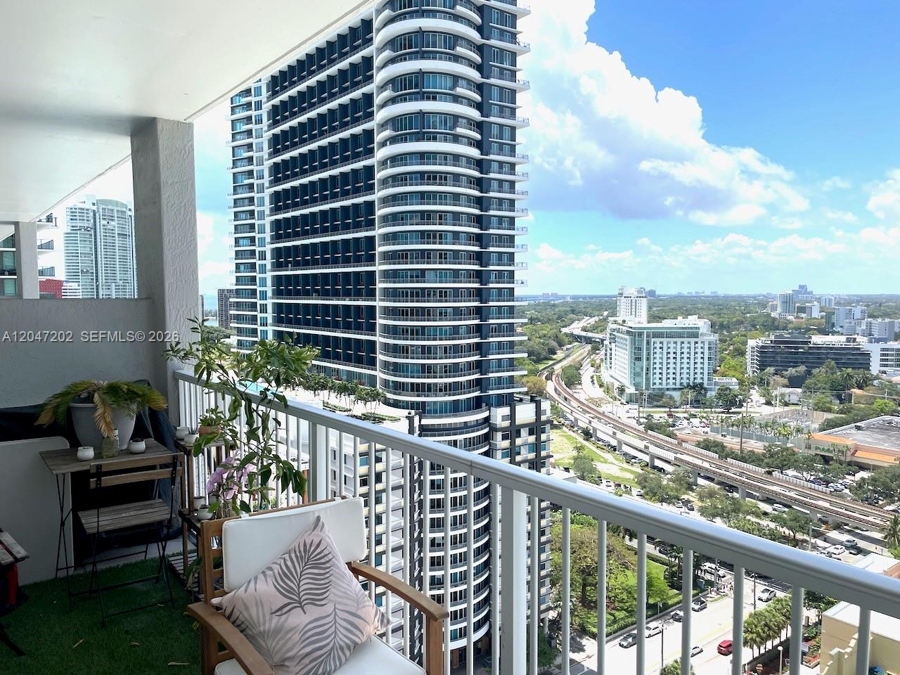 A balcony with a small table, chair, and potted plants overlooks a city skyline — 1250 S Miami Ave # 2111, Miami FL 33130, MIAMI, FL