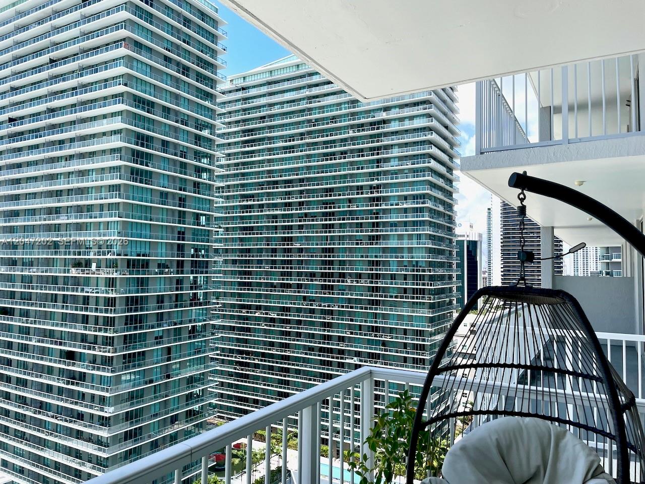 A balcony view features a hanging chair overlooking two tall, modern glass apartment buildings — 1250 S Miami Ave # 2111, Miami FL 33130, MIAMI, FL