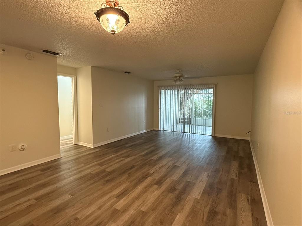 An empty living room features wood-look flooring, a ceiling fan, and sliding glass patio doors — 702 COUNTRY LANE NE UNIT 702, WINTER HAVEN, FL