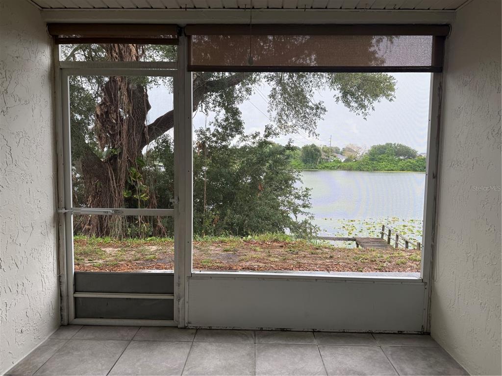 A screened-in porch with tiled flooring overlooks a lake and a wooden dock — 702 COUNTRY LANE NE UNIT 702, WINTER HAVEN, FL