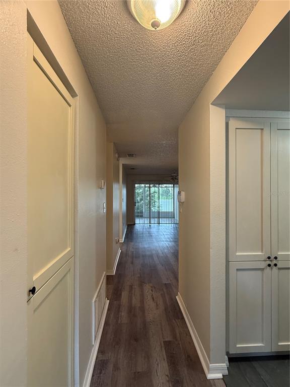 A hallway with wood-look flooring leads toward a sliding glass door with a view outside — 702 COUNTRY LANE NE UNIT 702, WINTER HAVEN, FL
