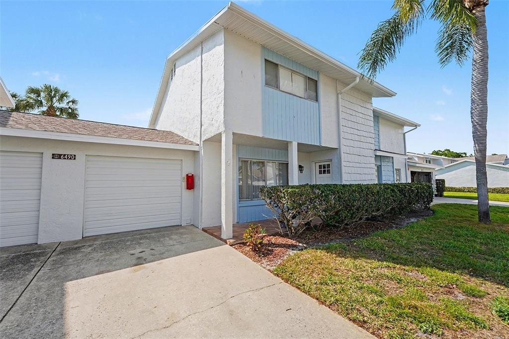 A two-story townhouse exterior features a white stucco facade, a garage, and a front porch — 6490 CAPE HATTERAS WAY NE UNIT 4, ST PETERSBURG, FL