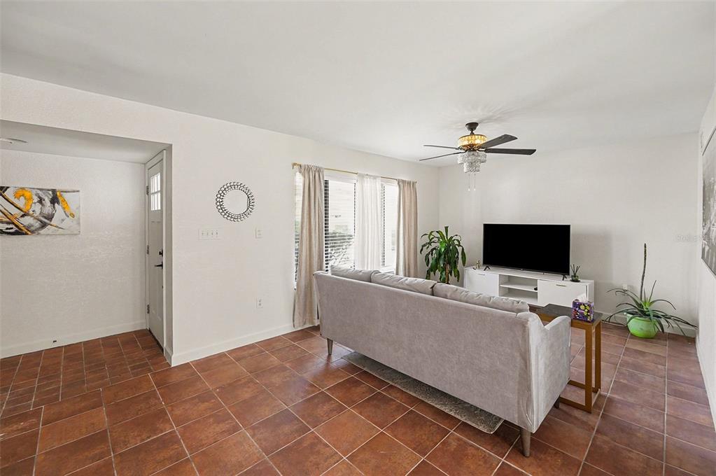 A living room with tile flooring, a gray sofa, a television, and a ceiling fan — 6490 CAPE HATTERAS WAY NE UNIT 4, ST PETERSBURG, FL