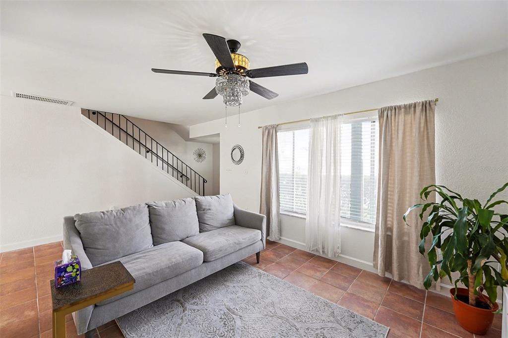 A living room features a gray sofa, tile flooring, a ceiling fan, and a staircase — 6490 CAPE HATTERAS WAY NE UNIT 4, ST PETERSBURG, FL