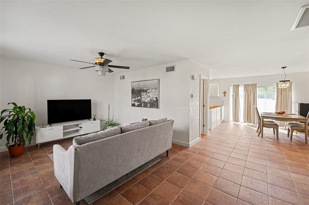 A living room and dining area with tiled floors, a grey sofa, and a television — 6490 CAPE HATTERAS WAY NE UNIT 4, ST PETERSBURG, FL