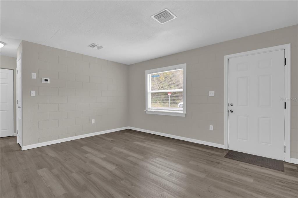 An empty room with gray block walls, wood-look flooring, a window, and a white door — 2307 MISPAH AVENUE UNIT A + B, LEESBURG, FL