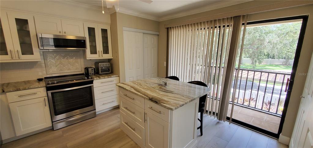 A kitchen features white cabinets, stainless steel appliances, a stone-topped island, and sliding glass doors — 6110 COUNTRY CLUB WAY UNIT 201, SARASOTA, FL