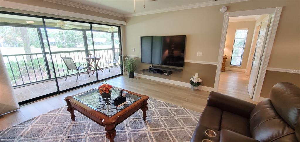 A living room features a wall-mounted television, a glass-topped coffee table, and a sliding glass door — 6110 COUNTRY CLUB WAY UNIT 201, SARASOTA, FL
