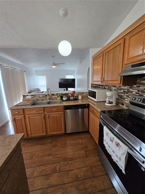 A kitchen features wood cabinets, stainless steel appliances, a tile backsplash, and wood-look flooring — 804 CARROUSEL LANE, KISSIMMEE, FL