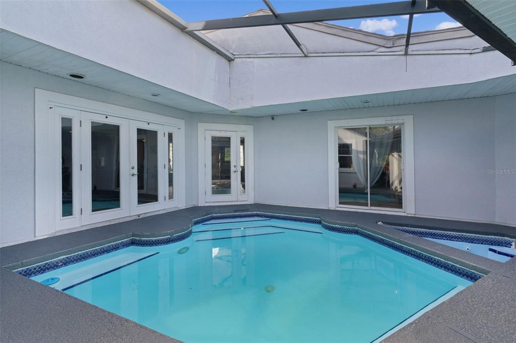 A screened-in swimming pool sits on a patio surrounded by white exterior walls and doors — 34415 KINGFISH STREET, FRUITLAND PARK, FL
