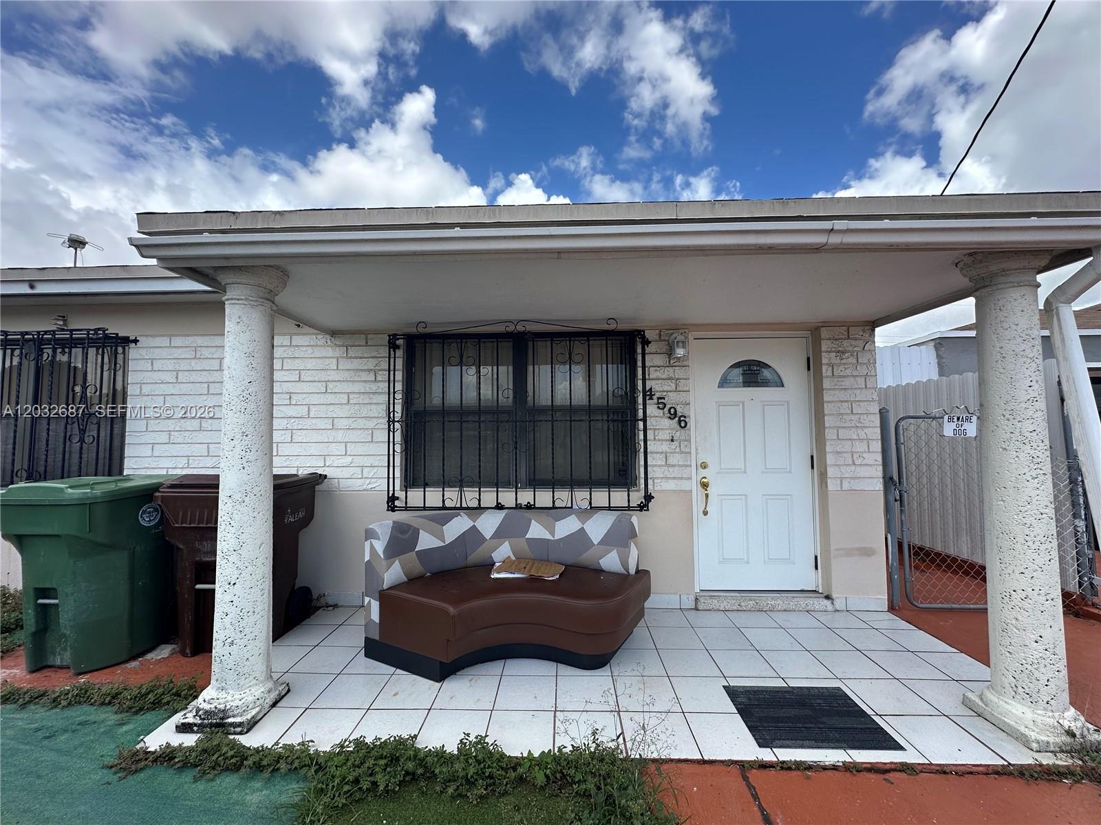 A covered front porch features white tiled flooring, two decorative columns, and a curved sofa — 4596 E 8th Ct, Hialeah FL 33013, HIALEAH, FL