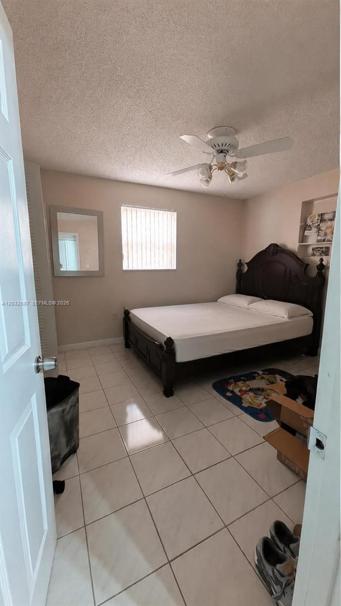 A bedroom features a dark wood bed frame, tiled floors, and a ceiling fan — 4596 E 8th Ct, Hialeah FL 33013, HIALEAH, FL