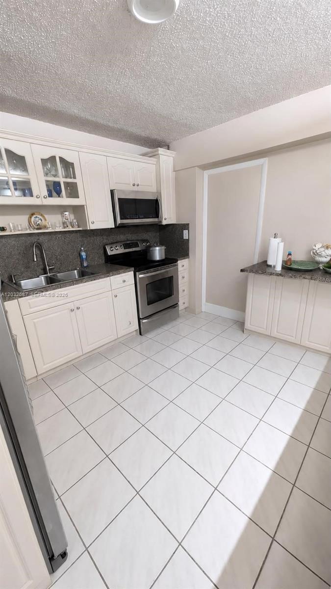 A kitchen features white cabinets, stainless steel appliances, and light-colored tile flooring — 4596 E 8th Ct, Hialeah FL 33013, HIALEAH, FL