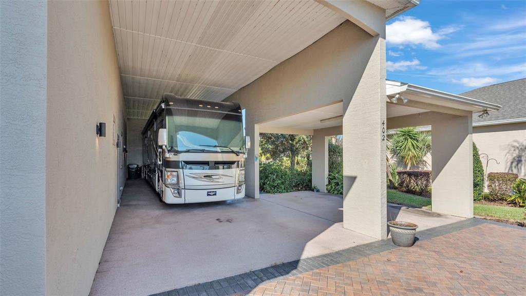 A large motorhome is parked under a covered carport attached to a residential house — 402 CRUISERS DRIVE, POLK CITY, FL