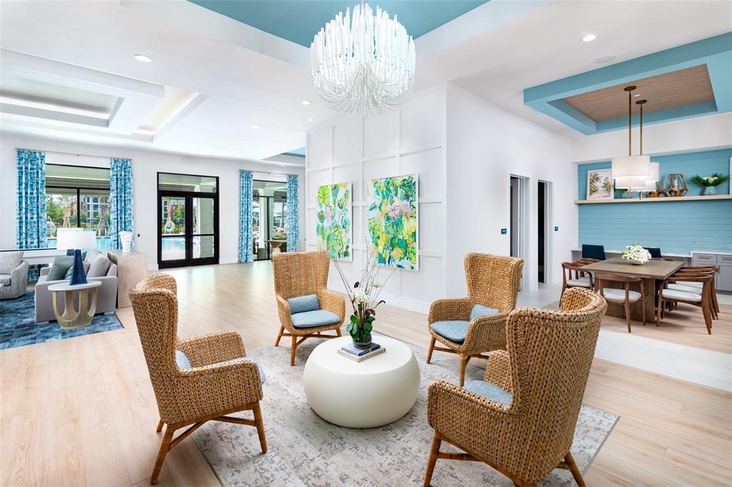 A bright, open-concept clubhouse lounge features wicker armchairs, a central coffee table, and blue accents — 100 WINDFLOWER LANE UNIT B2, DAYTONA BEACH, FL