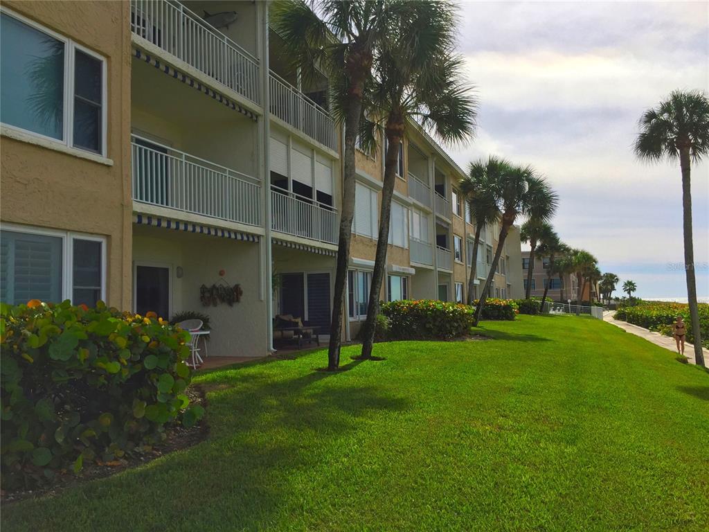 A multi-story apartment building with balconies overlooks a grassy lawn and palm trees — 3400 GULF BOULEVARD UNIT 108, BELLEAIR BEACH, FL